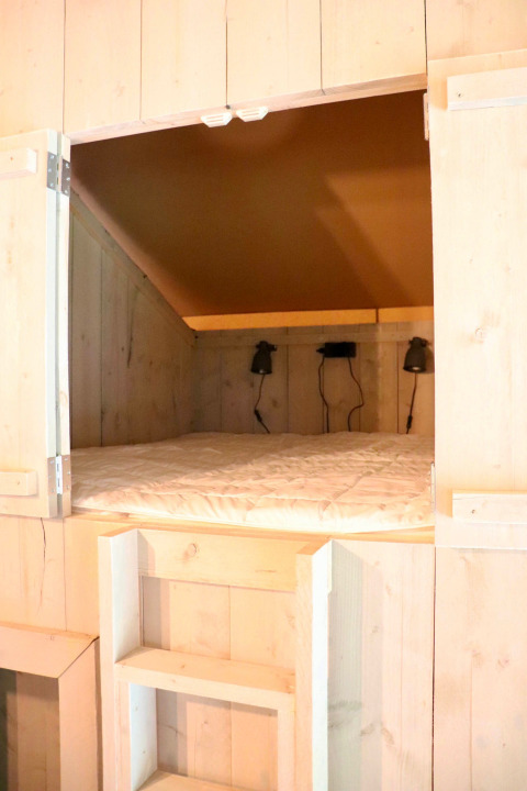Acogedora cama empotrada con paredes de madera y lámparas en tienda glamping de Tolne Camping, Dinamarca.