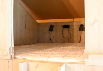 Acogedora cama empotrada con paredes de madera y lámparas en tienda glamping de Tolne Camping, Dinamarca.