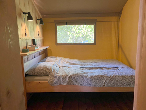 Interior view of a glamping tent at Tolne Camping in Denmark with a bed and window facing greenery.