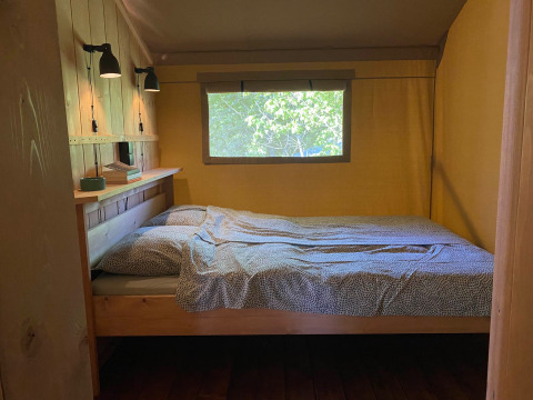 Binnenzicht van een glampingtent op Tolne Camping in Denemarken met bed en raam op het groen.