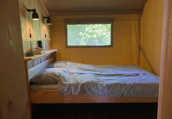 Vista interior de una tienda glamping en Tolne Camping, Dinamarca, con cama y ventana hacia la naturaleza.