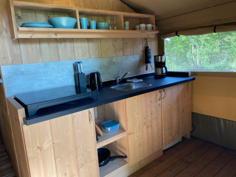 Cocina interior en tienda glamping con gabinetes de madera, fregadero y cafetera en Tolne Camping, Dinamarca.