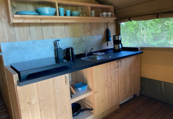 Cocina interior en tienda glamping con gabinetes de madera, fregadero y cafetera en Tolne Camping, Dinamarca.