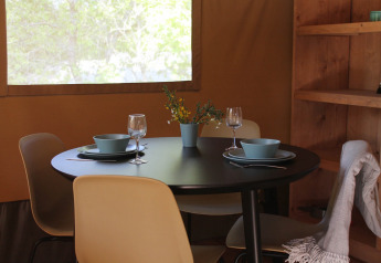 Mesa de comedor en una tienda glamping en Tolne Camping, Dinamarca, con vajilla, copas y flores.