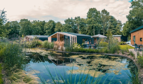 Vakantiepark met glampingverblijven aan een vijver, omringd door groen en genietende bezoekers.