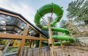 Gran tobogán acuático verde junto a edificio acristalado en parque de vacaciones con alojamiento glamping.