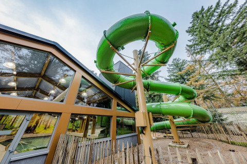 Gran tobogán acuático verde junto a edificio acristalado en parque de vacaciones con alojamiento glamping.