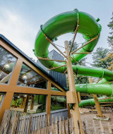 Grote groene waterglijbaan naast glazen gebouw in een vakantiepark met glamping-accommodaties.
