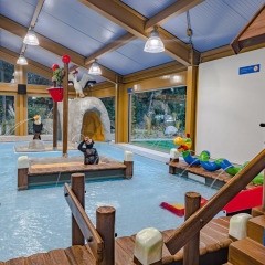 Overdekte speelruimte met peuterbadje en waterspeeltoestellen in een vakantiepark met glamping.