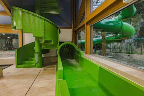 Grüne Wasserrutsche, die von drinnen nach draußen führt, in einem Ferienpark mit Glamping-Angeboten.