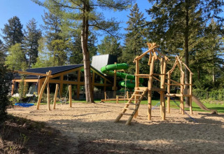Playground with wooden climbing frames and slide at a holiday park glamping site surrounded by forest.