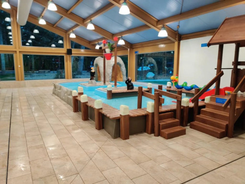 Piscina infantil cubierta con zona de juegos y tobogán en un parque vacacional con opciones de glamping.