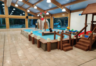 Indoor children's pool with play area, slide, and glamping accommodations at a family-friendly holiday park.