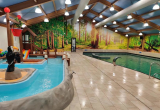 Piscine intérieure dans un parc de vacances avec fresque murale de forêt et espace aquatique pour enfants.