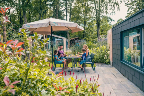 Gezin eet buiten onder een parasol aan een glampingaccommodatie in een vakantiepark.