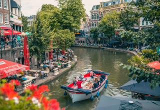 Gezellige drukte op terrasjes langs het water met een bootje dat door het centrum van een charmante stad vaart.