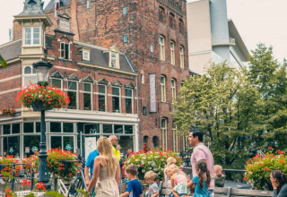 Familier og børn nyder en dag i en feriepark med glamping, omgivet af blomster og historiske bygninger.
