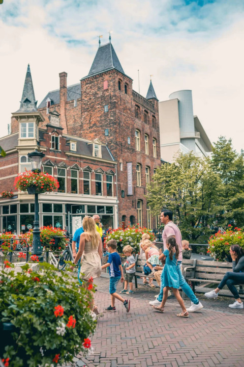 Familier og børn nyder en dag i en feriepark med glamping, omgivet af blomster og historiske bygninger.