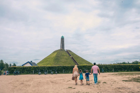 Familia camina hacia colina piramidal con torre en parque de vacaciones que ofrece glamping, día nublado.