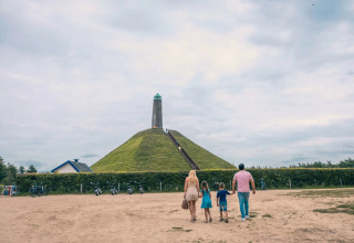 Gezin wandelt naar piramideheuvel met toren, bij vakantiepark met glamping in groene omgeving.