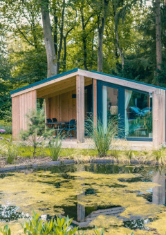 Moderne glampinglodge met terras en vijver, gelegen in een bosrijke vakantiepark omgeving.