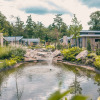 Holiday park with modern glamping cabins, landscaped pond and fountain, surrounded by lush greenery.