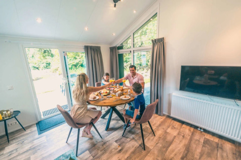 Family enjoying breakfast together in a modern glamping accommodation with large windows and garden view.