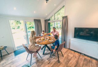 Famille prenant le petit-déjeuner dans un hébergement glamping moderne avec grandes fenêtres sur la nature.