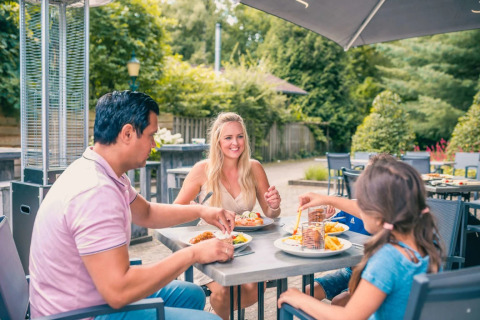 A family enjoys an outdoor meal at a holiday park with glamping accommodations, surrounded by greenery.