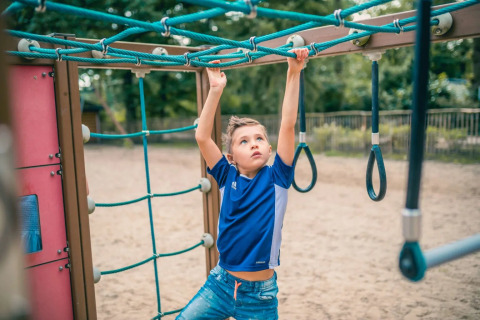 Niño jugando en la estructura de un parque infantil en un camping con opciones de glamping y naturaleza.