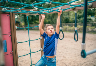 Jongen speelt op het klimrek in een vakantiepark met glamping faciliteiten in een groene omgeving.