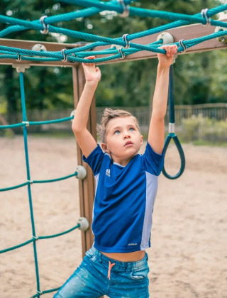 Jongen speelt op klimrek in vakantiepark met glamping accommodaties en veel buitenplezier.