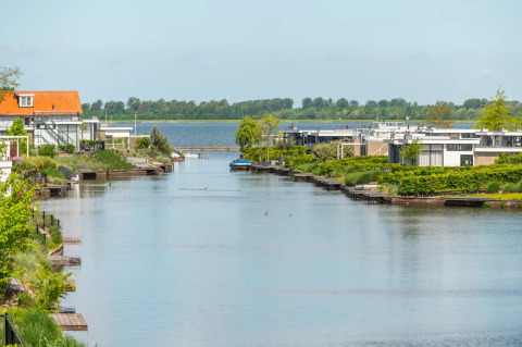 Vue d’un canal avec des logements de glamping modernes et de la verdure dans un parc de vacances.