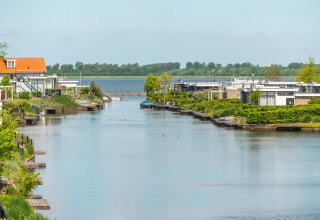 Vue d’un canal avec des logements de glamping modernes et de la verdure dans un parc de vacances.