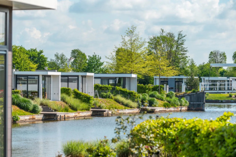 Modernos alojamientos glamping junto al agua en un parque vacacional rodeados de vegetación.