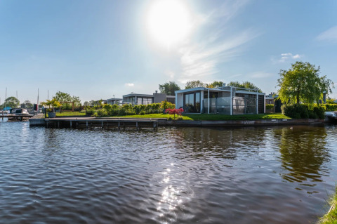 Cabañas modernas de glamping junto al lago en un parque vacacional, rodeadas de naturaleza y sol.