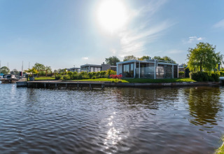 Moderne glampingverblijven aan een meer in een vakantiepark, omringd door zon en groen landschap.