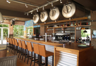 Bar moderno con tanques de cerveza y taburetes altos en un parque vacacional, ideal para glamping.