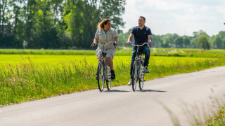 Dos personas pasean en bicicleta por un camino rural junto a un parque vacacional con glamping incluido.