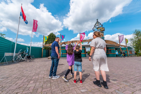 Une famille arrive à l'entrée d'un parc de vacances proposant du glamping sous un ciel ensoleillé.