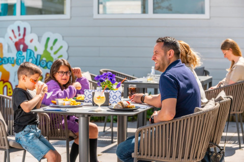 Familia almorzando al aire libre en un parque de vacaciones con glamping, niños comiendo y ambiente soleado.