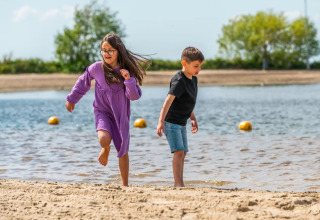 Deux enfants jouent sur la plage d’un parc de vacances avec hébergements glamping, profitant du beau temps.