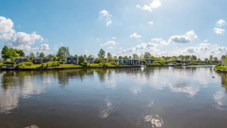 Vista panorámica de un parque vacacional con alojamientos glamping, cabañas modernas y lago tranquilo bajo el cielo azul.