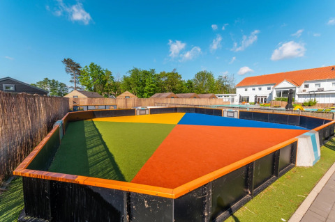 Campo polideportivo colorido en un parque vacacional con cabañas glamping y entorno soleado.