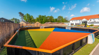 Campo polideportivo colorido en un parque vacacional con cabañas glamping y entorno soleado.
