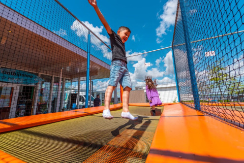 Niños saltando y jugando en una cama elástica en un parque vacacional con alojamiento tipo glamping.