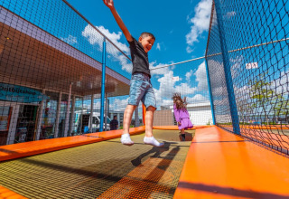 Børn hopper og leger på en trampolin under blå himmel i en ferielejr med glamping muligheder.