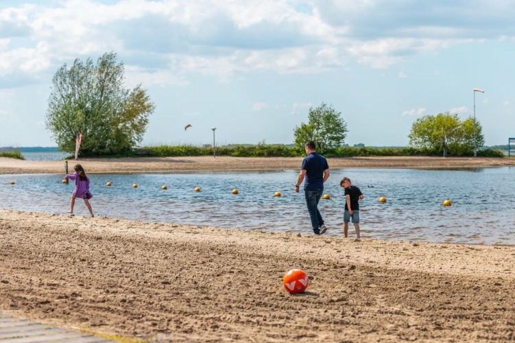 Familie verbringt Zeit am Sandstrand eines Ferienparks mit Glamping; Kinder spielen nahe dem Wasser.