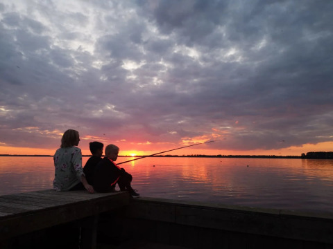 Familia pescando junta al atardecer en un muelle, disfrutando la vista al lago en un parque de glamping vacacional.
