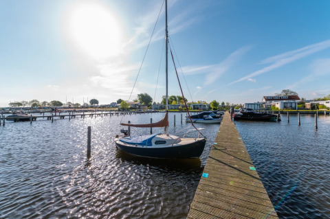 Zonnige dag bij vakantiepark haven met zeilboot aan steiger en glamping accommodaties op de achtergrond.